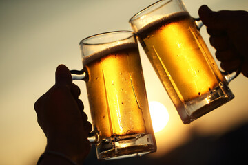 夕日を背景にビールで乾杯するジョッキと手もとアップ