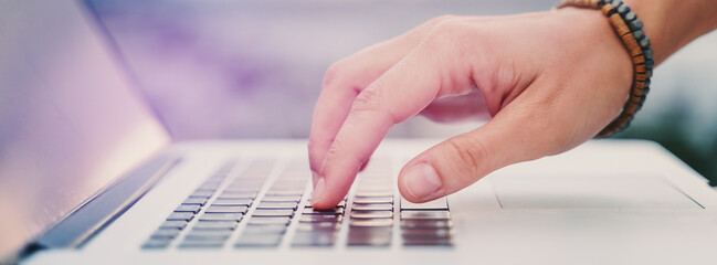 Close-up of hands typing on laptop keyboard in the office. Banner format