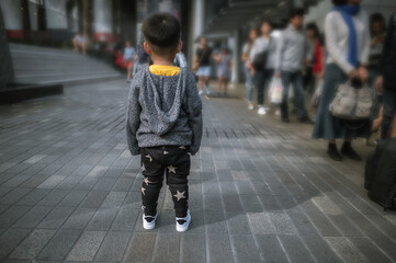 Small kid standing alone in big city while group of people walking in the street