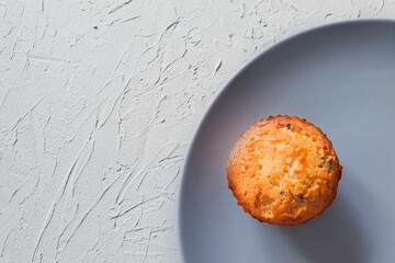 The focus of the photo is on the right on a delicious cupcake. Soft focus background. The cupcake lies on a round dark gray plate, which is on a concrete gray background. View from above.