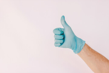 Closeup man doctor show thumb up sign with hand in medical latex glove isolated on white background. Male hand in blue protective glove gesture agreement like ok. Advice, recommend, alright, COVID-19