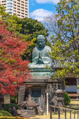 Bronze statue of Buddha Shaka Nyorai with a stone lantern and the sentence May Peace Prevail On Earth on a Peace Pole Project's pole in the Tennoji temple of Yanaka.