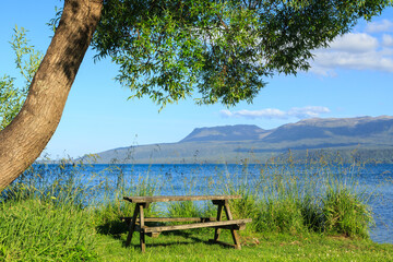A picnic area with a table on the shore of Lake Tarawera, New Zealand. In the background is Mount Tarawera, a dormant volcano