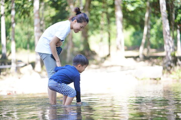 Mother and son playing water on shallow canal during family vacation in summer time 