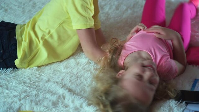 A little girl interferes with homework the boy. Books are lying on the bed.Children have play in bed, the boy tickles the girl and laughs.