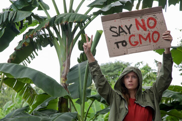 Save NO to GMO. Caucasian woman holding a cardboard sign against genetically modified organisms and...