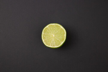 Closeup overhead view of half cut lime on abstract black background with copy space.