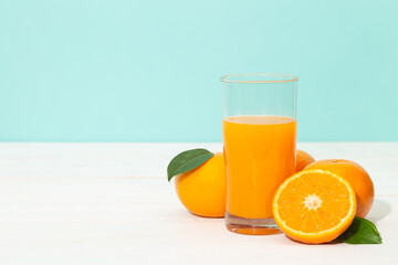 Fresh orange juice in glass and oranges fruit on white wooden table with blue background with copy space.