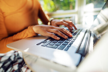 Closeup of woman surfing on internet while sitting in cafe. Hands are on keyboard.