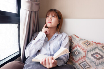Closed up image of an asian woman reading a book comfortably. Isolating at home.