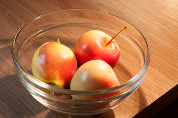 ripe bright apples in a glass plate close-up on a wooden table
