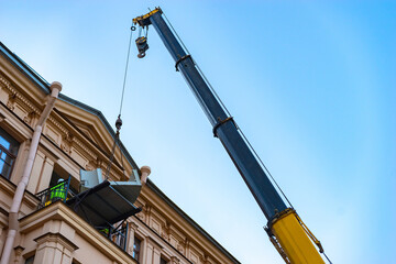 Fototapeta na wymiar Crane. Repair work in a historic building. Loading oversized materials to the apartment. A crane lifts furniture into the apartment. Truck crane. Construction work at height. Reconstruction.