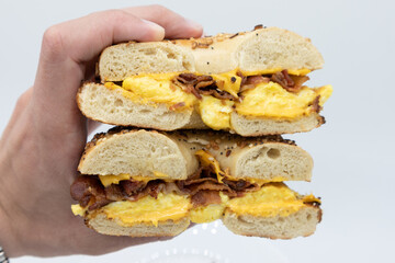 Hand Held Everything Bagel Cut in Half with Bacon Eggs and Cheese with a White Background