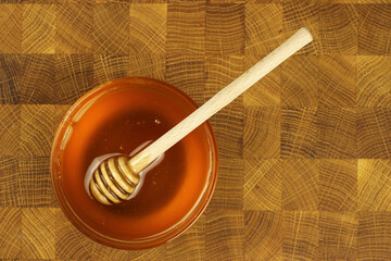 Honey in a bowl with a stick on a wooden Board