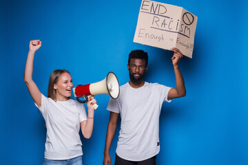 Young caucasian woman with megaphone and African man holding a cardboard poster with the message...