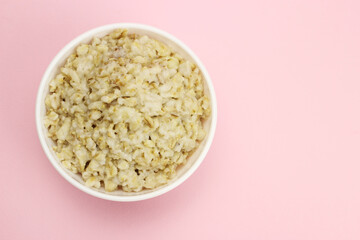 Bowl of oats porridge on a pink background. Healthy breakfast