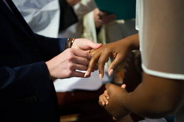 Obraz na płótnie Canvas White man and black woman are getting married in a church, exchanging rings. A Child's hand is holding brides hand too. Black lives matter, equality concept.