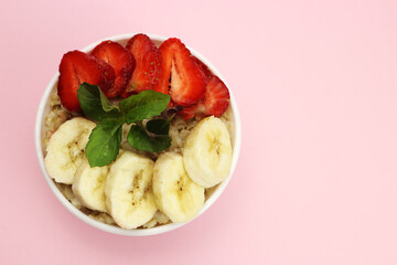Bowl of oatmeal with fruit on a pink background. Healthy breakfast