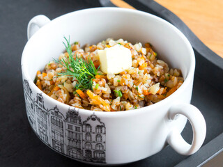Buckwheat with vegetables in a white bowl. Garnished with a sprig of parsley. Serving porridge