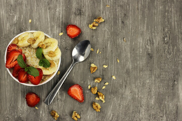 Bowl of oatmeal with a banana, strawberries and mint on a gray background. The view from the top. Fresh healthy Breakfast