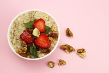 Bowl of oatmeal with fruit and walnuts on a pink background. Healthy breakfast