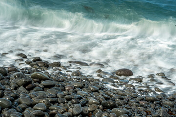 Waves crashing on pebble beach with slow shutter speed. Artistic effect.