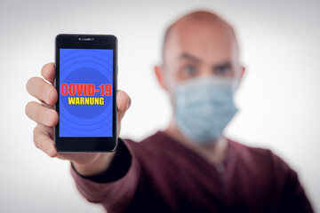 Mann mit Maske hält Mobiltelefon mit covid-19 app in der Hand