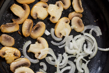 Fried sliced champignons with onions in a pan. Mushrooms with onions in a pan. Cooking lunch and dinner. Fried onion rings