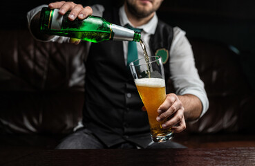 A man pours light wheat beer from a bottle into a glass, bubbles and foam. Gentleman in a vest and shirt