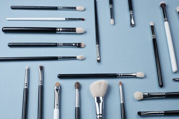 brushes for make-up or drawing white and black of different sizes lie in different directions on a blue background.