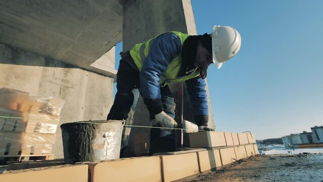 One man lays bricks on a wall in building.