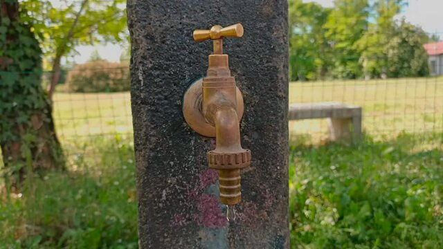 un rubinetto di una fontana nel parco goggiola  e si sentono gli uccellini cantare