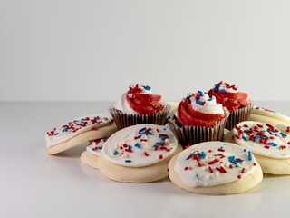 Patriotic baked goods, sugar cookies covered with white frosting and red, white and blue sprinkles with mini chocolate cupcakes with red and white frosting and star sprinkles.