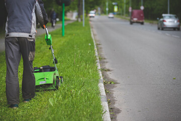 A worker in protective clothing and gloves with a gasoline mower on wheels walks along the lawn...