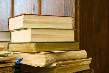 Old books stacked upon one another against an oak paneled background