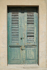 Green shuttered doors with peeling paint with bright sunshine casting deep shadows