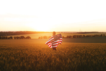 Beautiful girl with American flag in a wheat field at sunset. 4th of July.  Independence Day,...