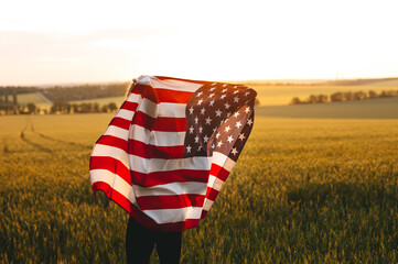 Beautiful girl with American flag in a wheat field at sunset. 4th of July.  Independence Day, Patriotic holiday.