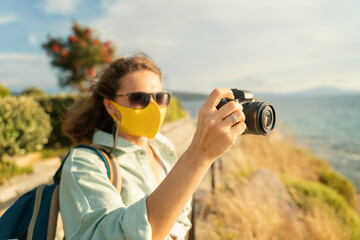 Fototapeta premium Cool beautiful happy girl woman traveler by the sea with a mask on her face, stylish outfit, with a camera in her hands