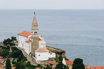 Saint George Cathedral in Piran with calm sea on the background and green trees nearby