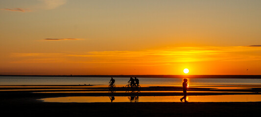 People walking on the beach at sunset.
