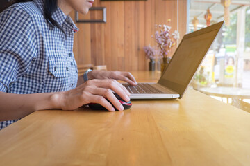 Woman's hand clicking on wireless mouse with laptop on wooden table.Female office worker clicking on mouse