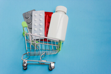 Shopping cart loaded with pills on blue background. The concept of medicine and the sale and delivery of drugs. Copy space