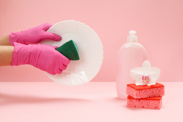 Women's hands in gloves with a sponge and a plate on the pink background.