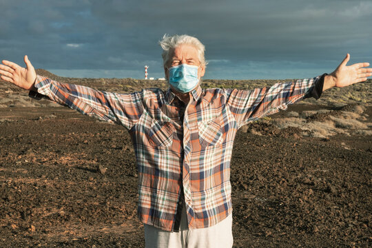 Senior man with medical face mask enjoying nature outdoors. Lighthouse at the horizon. Partial conquest of freedom after coronavirus lockdown