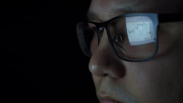 Reflection of the cryptocurrency chart in the businessman's glasses. The Eastern investor follows the cryptocurrency schedule. Reflection of the graph in the glasses of an Asian man