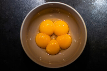 Five egg yolks in a bowl on black kitchen top