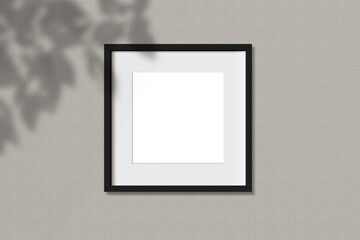 Minimal empty square black frame picture mock up hanging on white wall background with leaves shadow. isolate image