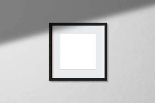 Minimal empty square black frame picture mock up hanging on white wall background with window light and shadow. isolate image