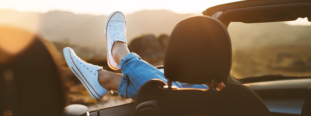 A young girl rests and pushes her shoes out of the convertible to enjoy the view
